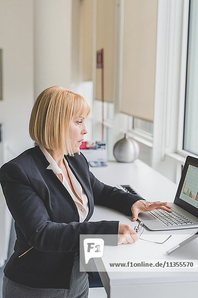 Mature businesswoman looking at bar graph on office laptop