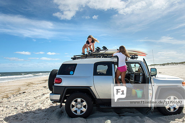 Two young girls untying surfboards from top of car