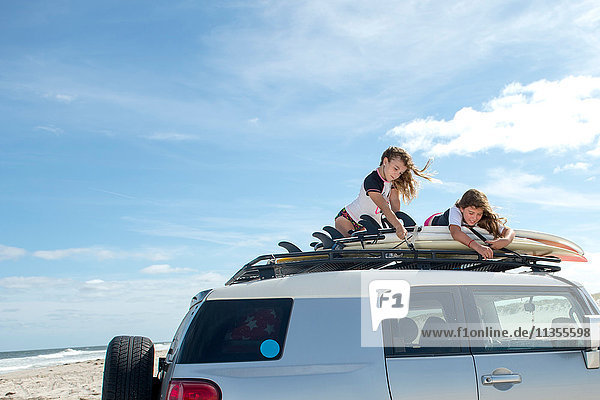 Zwei junge Mädchen sichern Surfbretter auf dem Autodach