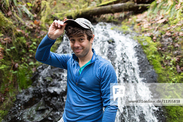 Man in front of waterfall wearing baseball cap looking at camera smiling