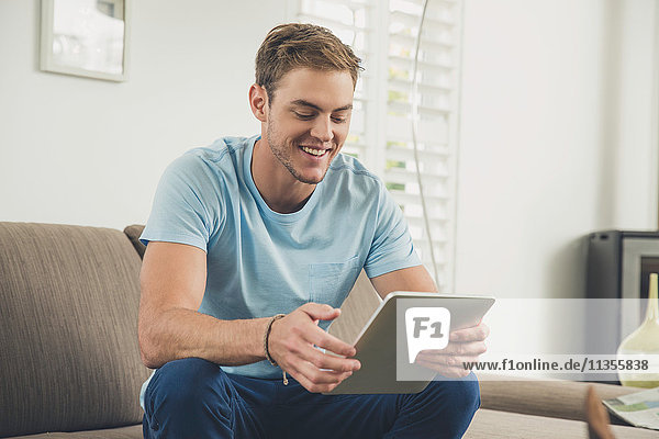 Mann auf Sofa mit digitalem Tablet lächelt