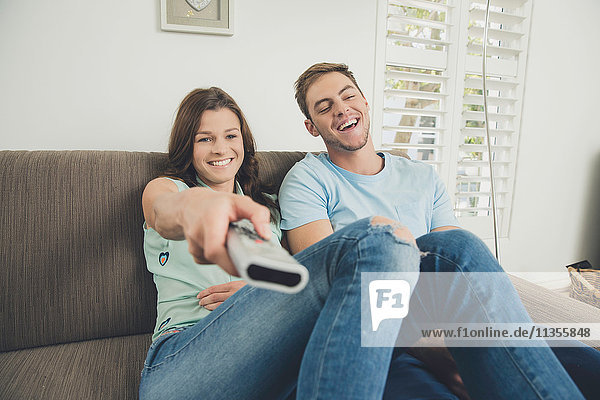 Couple on sofa using remote control smiling