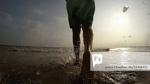 Beine einer Frau an der Küste beim Spaziergang im Meer