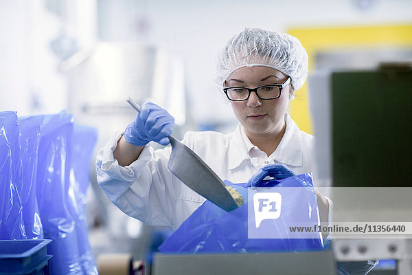 Fabrikarbeiter schaufelt Lebensmittel in blaue Plastiktüten