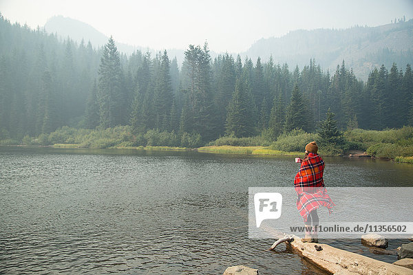 In Schottenkaro-Decke gehüllte Frau trinkt Kaffee am nebligen See  Mount Hood National Forest  Oregon  USA