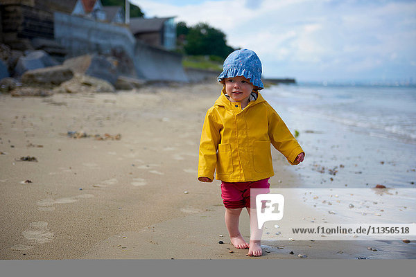Baby girl on beach wearing sunhat and raincoat