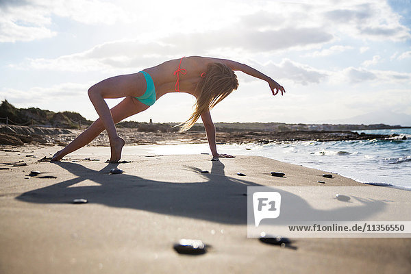 Junge Frau am Strand  in Yogastellung  Rückansicht