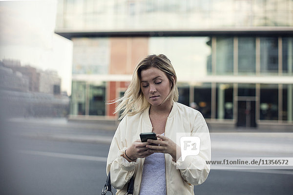 Junge Frau mit Handy gegen Bauen in der Stadt