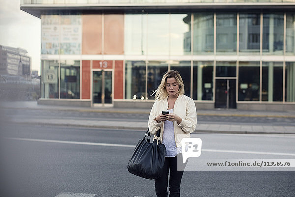 Junge Frau beim Spaziergang auf der Stadtstraße mit dem Handy