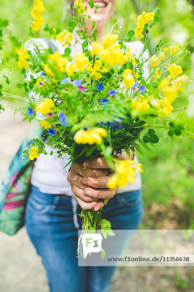 Schnappschuss einer Frau  die einen Strauss frischer gelber Wildblumen im Garten hält