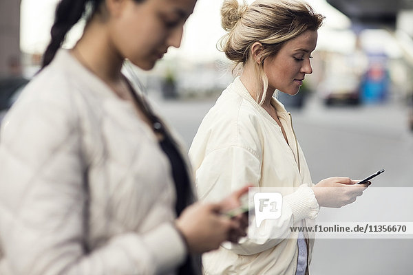 Seitenansicht von jungen Frauen mit Mobiltelefonen in der Stadt