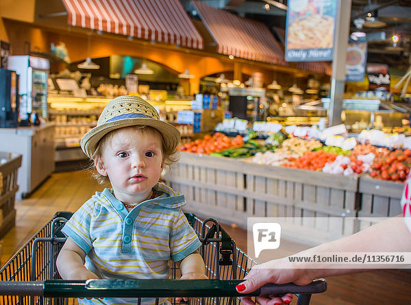 Kleiner Junge mit Strohhut im Einkaufswagen sitzend