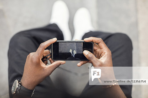 High angle view of man photographing legs on mobile phone