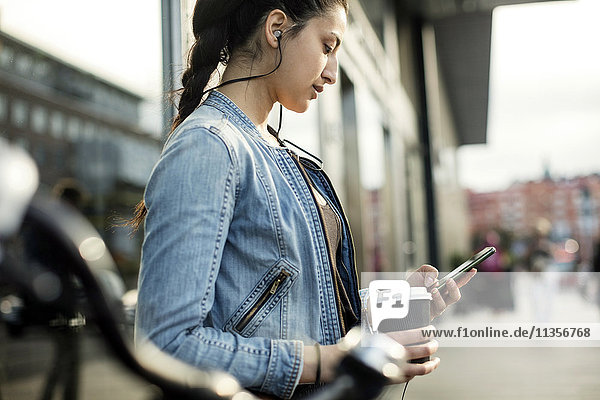 Seitenansicht der Frau mit Smartphone und Kaffeetasse in der Stadt