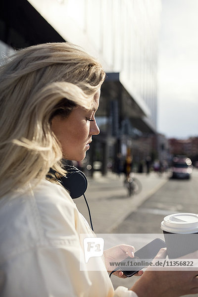 Seitenansicht der Frau mit dem Handy beim Halten der Kaffeetasse in der Stadt