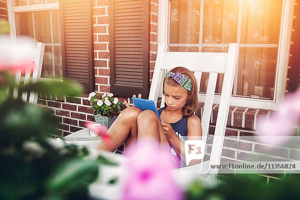 Mädchen auf der Veranda im Schaukelstuhl mit digitalem Tablet