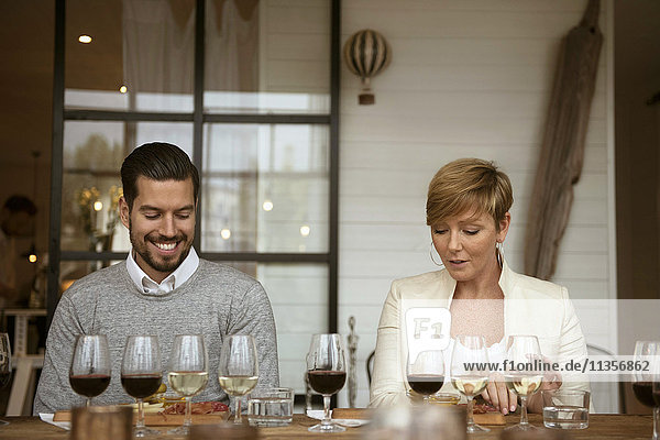 Lächelnde Geschäftsleute bei der Analyse von Weingläsern am Tisch