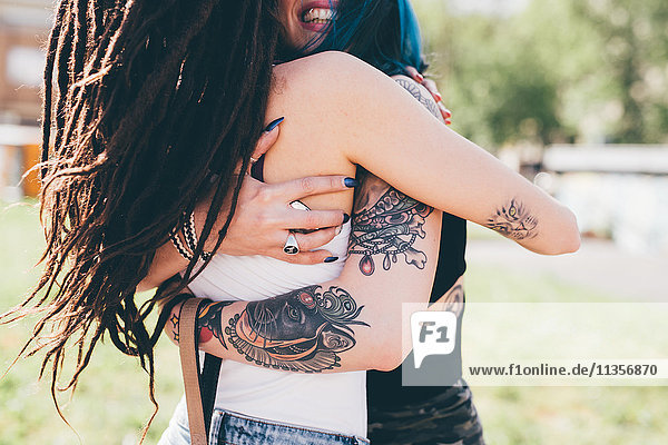 Tätowierte junge Frauen umarmen sich im Stadtpark