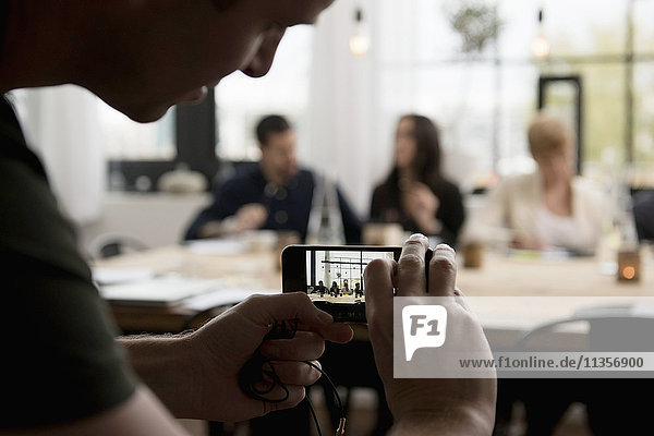 Man photographing business people through mobile phone at office