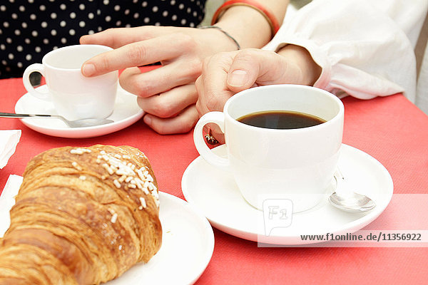 Nahaufnahme von Frauenhänden bei schwarzem Kaffee und Croissants im Strassencafé