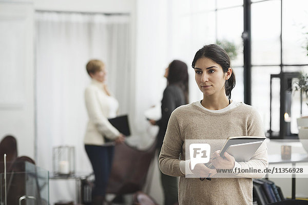 Thoughtful businesswoman holding laptop with colleagues in background