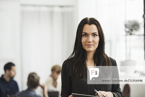 Portrait of businesswoman standing with people in background