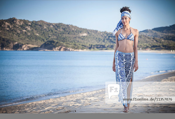 Hübsche junge Frau in Bikini-Oberteil und Sarong beim Strandspaziergang  Costa Rei  Sardinien  Italien