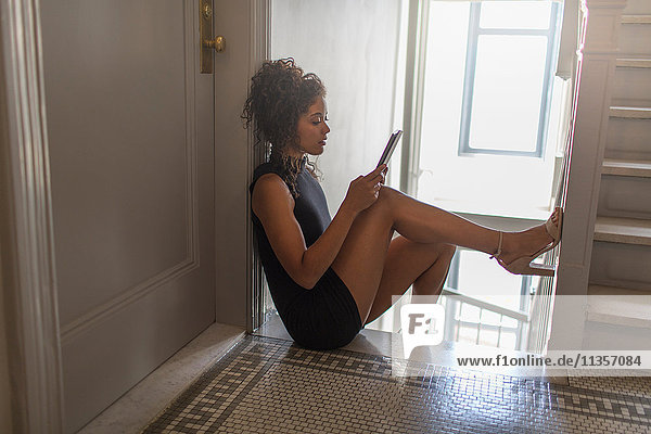 Junge Frau sitzt oben auf der Treppe und benutzt ein digitales Tablett