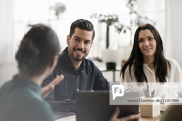 Smiling colleagues looking at businesswoman showing laptop during meeting