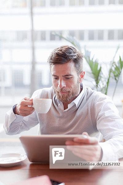Reifer Mann sitzt im Café  trinkt Kaffee und benutzt ein digitales Tablett