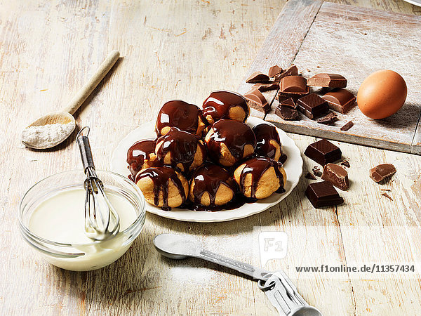 Profiteroles mit heisser Schokoladensauce  Sahnefüllung in Schüssel mit Schneebesen  Holzlöffel mit Mehl  Ei  Zucker in Messlöffel  Schokoladenstücke