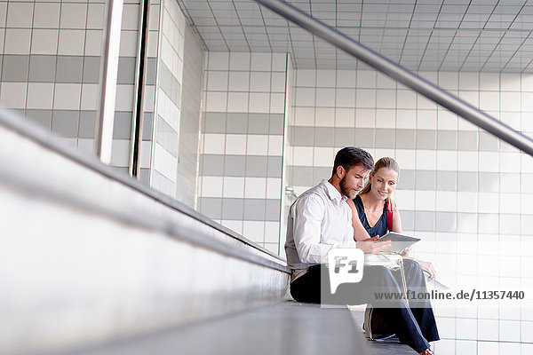 Reifer Mann und Frau sitzen auf Stufen und schauen auf ein digitales Tablett