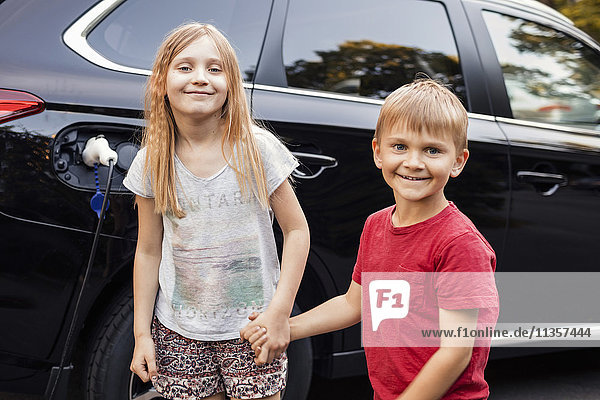 Porträt eines glücklichen Mädchens und Jungen gegen ein schwarzes Elektroauto