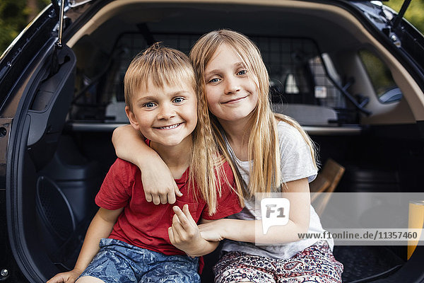 Portrait of happy girl and boy sitting in car trunk