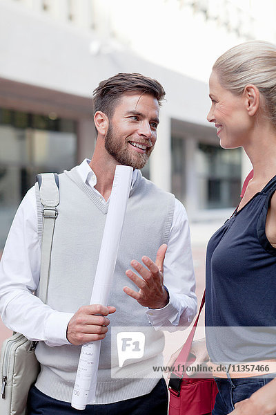 Mature man and woman outdoors  having discussion  man holding rolled up documents