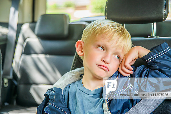 Young boy sitting in back of vehicle  bored expression
