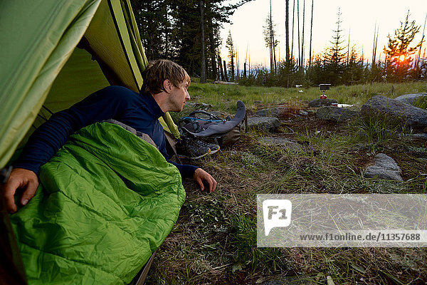 Male camper in sleeping bag watching sunset on Midnight Ridge  Colville National Forest  Washington State  USA