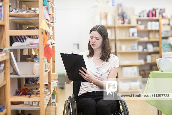 Young female shop assistant using wheelchair stocktaking in shop
