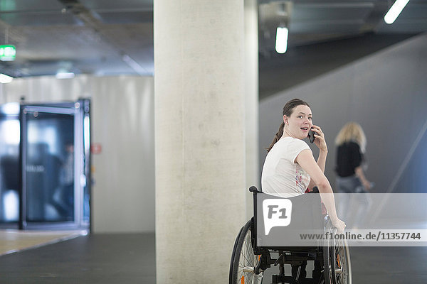 Young woman using wheelchair in underground parking lot talking on smartphone