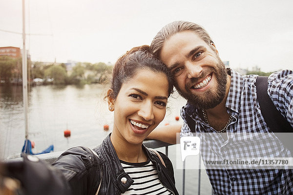Portrait of smiling couple standing by river in city against clear sky