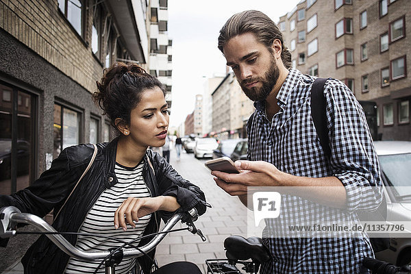 Man showing phone to female friend with bicycle at sidewalk in city
