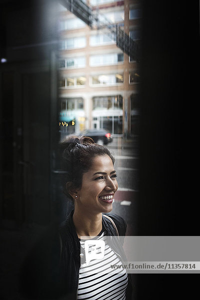 Lächelnde Frau steht in der Stadt durchs Fenster gesehen