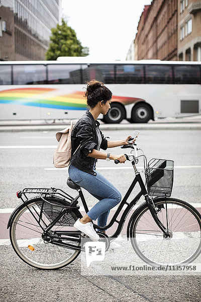 Seitenansicht der Frau mit dem Handy beim Radfahren auf der Stadtstraße