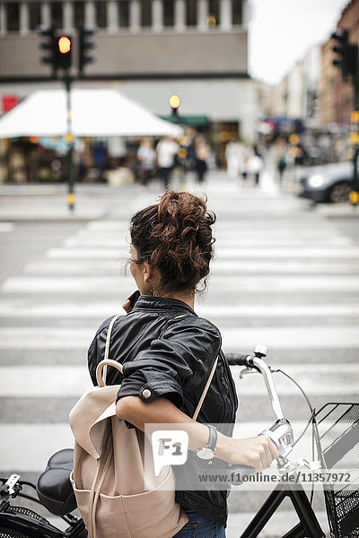 Frau mit Fahrrad stehend auf Zebrastreifen in der Stadt