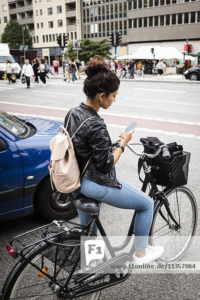 Volle Länge der Frau mit dem Fahrrad mit dem Handy  während sie an der Stadtstraße steht.