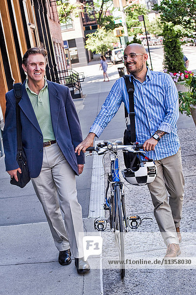 Geschäftsleute gehen auf der Straße  mittelgroßer Mann schiebt Fahrrad  lächelnd