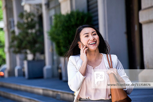 Geschäftsfrau  die im Freien geht  ein Smartphone benutzt und lächelt