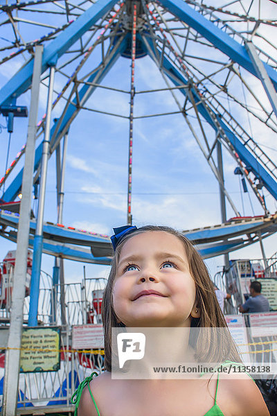 Cute girl looking up in front of ferris wheel at amusement park