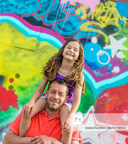 Portrait of girl on father's shoulders in front of wall mural at amusement park