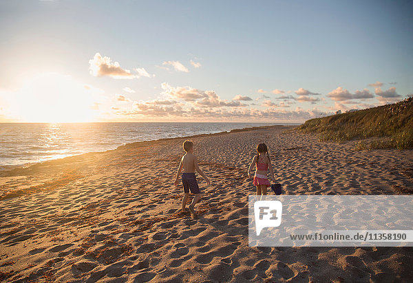 Junge und Schwester spazieren bei Sonnenaufgang am Strand entlang  Blowing Rocks Preserve  Jupiter Island  Florida  USA